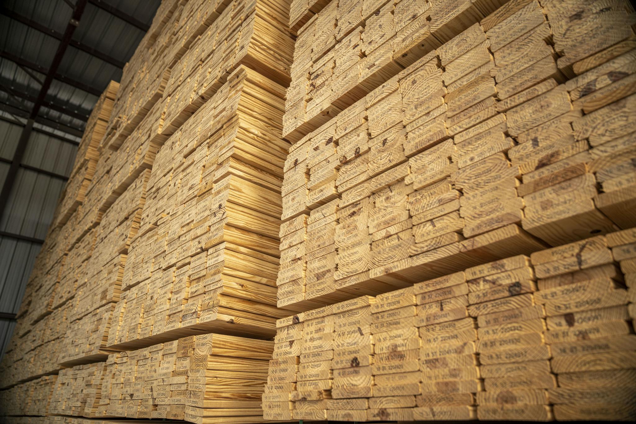 Large stacks of lumber stored in an industrial warehouse, showcasing woodworking materials.