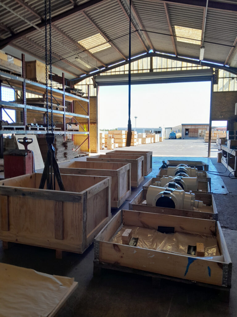 Littoral Caisserie -Intérieur d'un hangar avec des caisses en bois, des équipements industriels et des chaînes de levage.