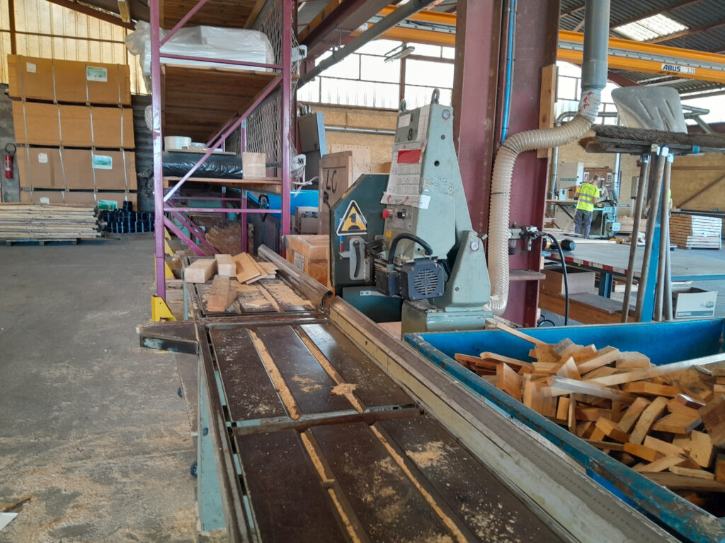 Machine industrielle de transformation du bois avec des planches et des copeaux dans un atelier.