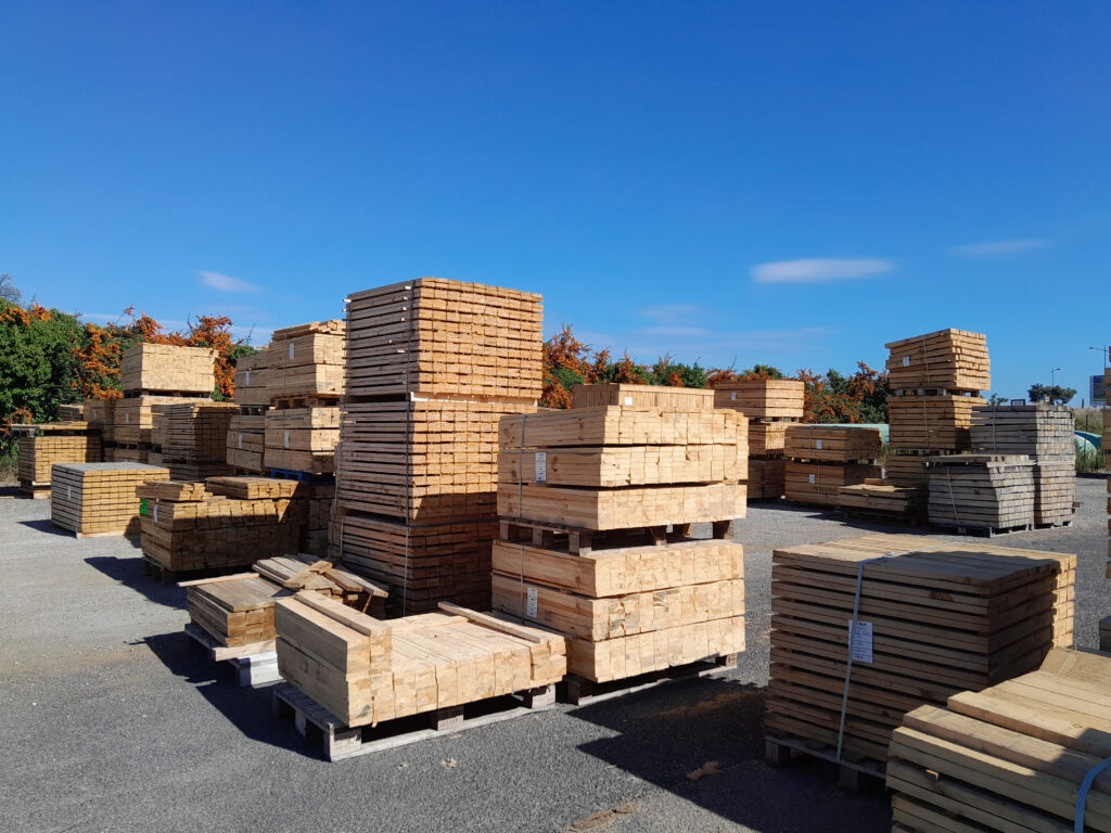 Grandes piles de planches de bois sciées et de palettes, stockées en extérieur sous un ciel bleu.