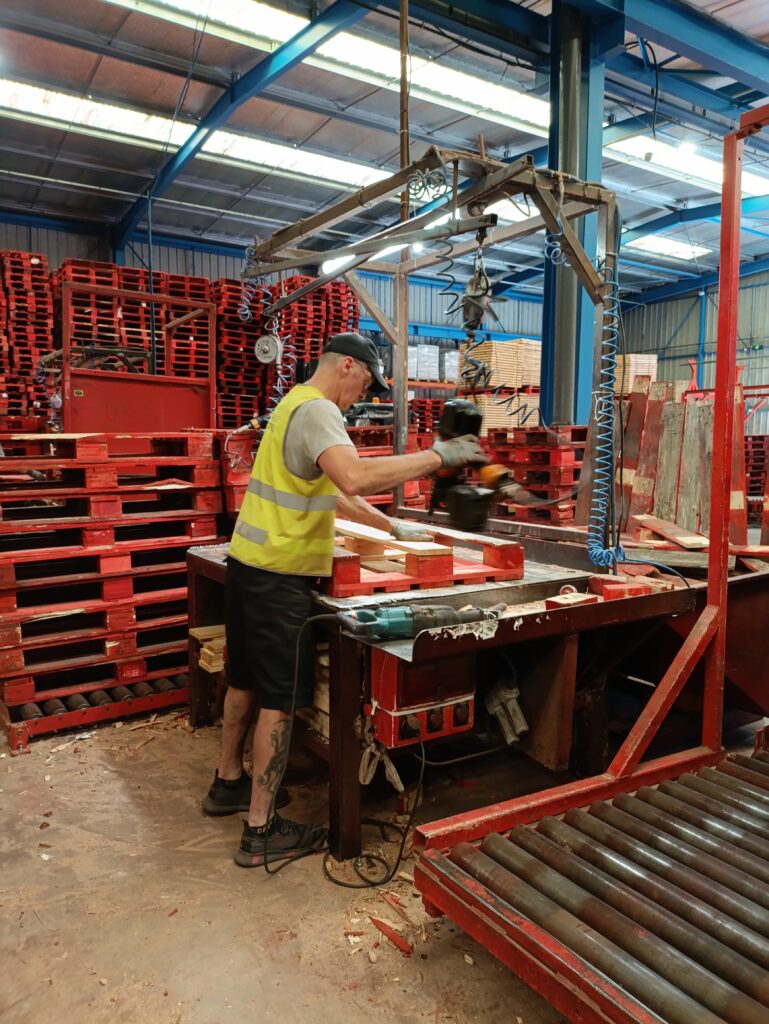 Un ouvrier en gilet de sécurité effectue la réparation d'une palette en bois dans un atelier.