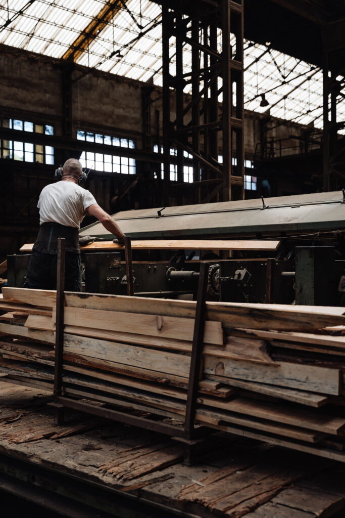 Intérieur d'un atelier de sciage avec machines à bois, stocks de planches et un opérateur.